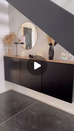 a black cabinet under a stair case in a room with white walls and grey flooring