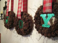 three wreaths are hung on the wall with green letters and red plaid ribbon around them