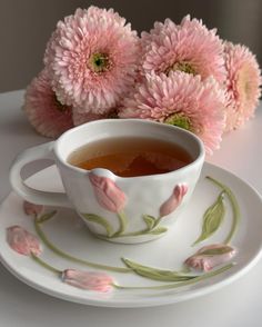 a tea cup and saucer with pink flowers in the background on a white plate