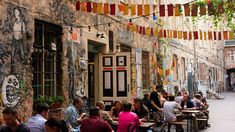 people sitting at tables in an alleyway with colorful streamers hanging from the ceiling