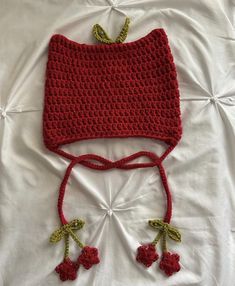 a crocheted red hat with green leaves on the top and bottom, sitting on a white sheet