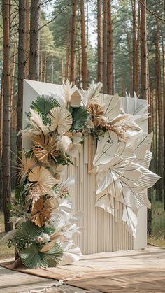 a white and gold wedding arch decorated with flowers, leaves and pineconis in the woods