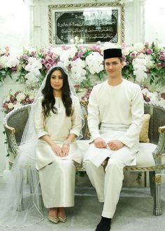 a man and woman sitting next to each other on a bench in front of flowers