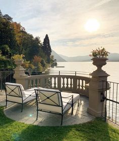 two lawn chairs sitting next to each other on top of a lush green field near the water