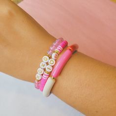 two bracelets on the arm of a person wearing pink and white beads with buttons