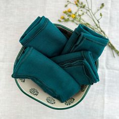 folded teal napkins sitting on a plate with flowers in the backgroung