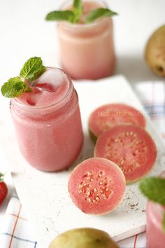 two jars filled with pink liquid and some sliced up strawberries next to each other