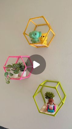 three hexagonal shelves with plants and toys on them hanging from the side of a wall