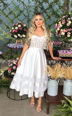 a woman is standing in front of some flowers and potted plants with her hands on her hips