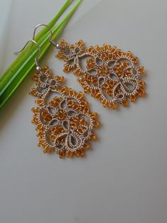 a pair of gold and silver earrings sitting on top of a white table next to a green plant