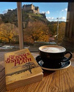 a cup of coffee sitting on top of a wooden table next to an open book