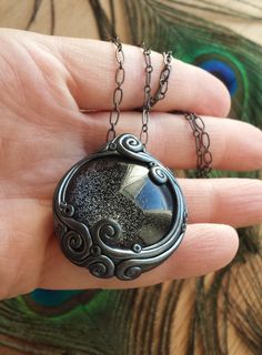 a hand holding a necklace with a black stone in the center and an intricate design on it