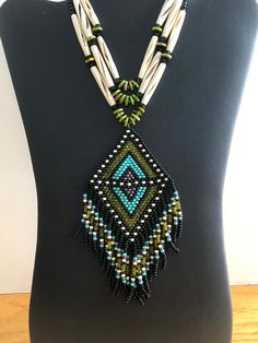 The pendant is made of black, cream, yellow green, turquoise and purple seed beads.  It is attached to 3 strands of turquoise stones, cream hairpipe, black crystals and glass seed beads. The necklace is finished with a black leather like cord and bronze  findings.  The ends are loosely tied so the length is adjustable. The finished length is about 15" now, but you can lengthen or shorten the ties to make any length that suits your outfit.  It can be worn as a pendant or as a choker. Weaving Necklace, Vert Turquoise, Necklace Bead, Turquoise And Purple, Cream Yellow, Necklace Beaded, Turquoise Stones, Jewelry Choker, Green Turquoise