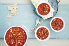 three bowls of chili with crackers and spoons on a blue wooden table top