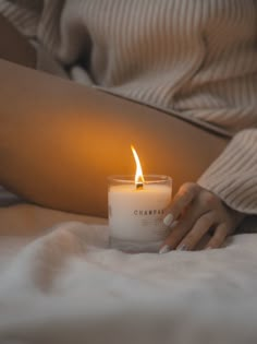 a woman laying in bed holding a candle with the light shining on her stomach behind her