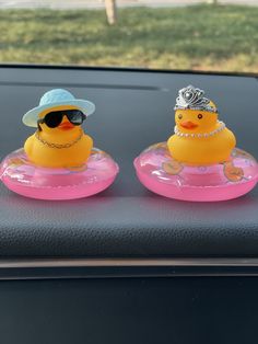 two rubber ducks wearing hats and sunglasses on top of a car dash board in the sun