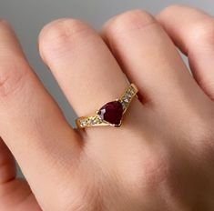 a woman's hand wearing a gold ring with a red stone and diamond accents