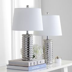 two lamps sitting on top of a white table next to a book and flower vase