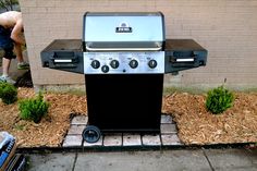 a bbq grill sitting on top of a sidewalk next to a brick wall and grass