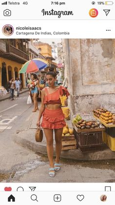 a woman walking down the street with an umbrella over her head and fruit on display behind her