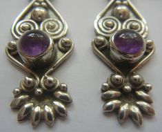 "Sterling silver and amethyst earrings. Vintage, handmade Bali earrings with a complex design of pebbles, swirls, spirals, pedal burst and cabochon stone. All the elements balance perfectly as the Balinese can so easily achieve. The design has a tribal bohemian look and will be a lot of fun to wear. The amethyst is slightly domed and the color is a nice deep purple. The back is solid and the ear wires are wrapped at the base. Nice weight without being too heavy and in excellent vintage condition Purple Bohemian Filigree Jewelry, Ornate Purple Sterling Silver Earrings, Bohemian Sterling Silver Clip-on Earrings, Silver Braided Ring, Vintage Amethyst Purple Earrings, Bohemian Silver Flower-shaped Earrings, Complex Design, Bali Jewelry, Bali Earrings