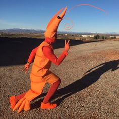 a man dressed in an orange costume is walking across the street with his arms out