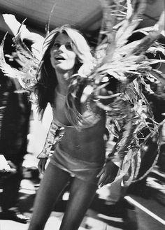 black and white photograph of a woman with feathers on her head walking down the street