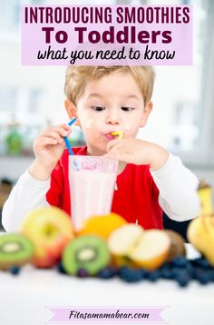 a young boy is eating fruit while sitting at a table in front of a cup