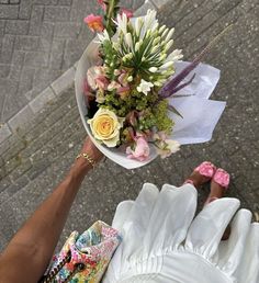 a person holding a bouquet of flowers in their hands on the sidewalk with other people's feet