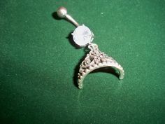 a small silver brooch with an ornate design on it's side, sitting on a green surface