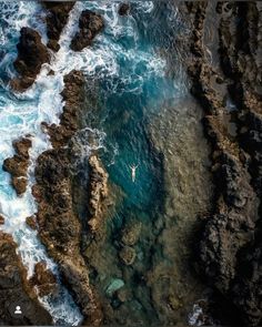 an aerial view of a person in a body of water surrounded by rocky coastlines