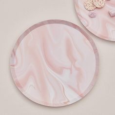 two pink marble plates sitting on top of a white table next to cookies and marshmallows