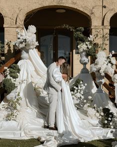 a bride and groom kiss in front of their wedding arch with flowers on the ground