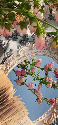 a mirror with pink flowers in it and a book on the table next to it