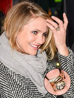 a woman wearing a scarf is smiling and holding her hand up to her head with both hands