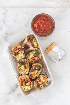 an overhead view of several burritos on a white tray with salsa in the background