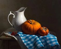 two oranges and a white pitcher sitting on a blue checkered cloth next to a tablecloth