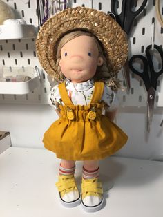 a doll with a straw hat and yellow dress is standing in front of some scissors