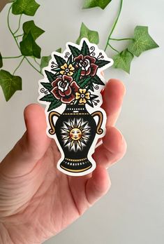 a hand holding a sticker with flowers in a vase