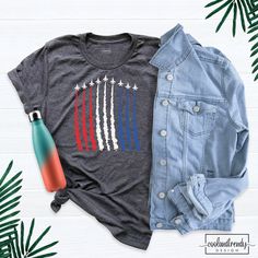 an american flag shirt, jean jacket and water bottle on a white wooden background with palm leaves