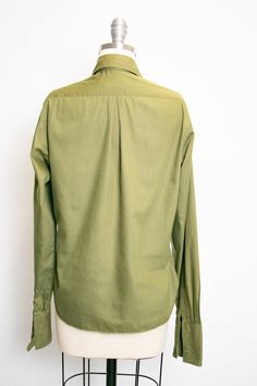 "Vintage 1950s ladies button down blouse in soft moss green cotton blend. Pointed collar. Relaxed yet feminine fit. Simple button front. Long sleeves that need cufflinks, not included. Unlined. Label: Adelaar man tailored shirt - Cotton + Darcon Fits like size: Medium Measurements: Bust: 38\" - 40\" pit tp pit Waist: 36\" Length: 22.5\" Shoulder to shoulder: 16\" Sleeve: 24\" Condition: Very good/good. Very minor under arm fade and a few faint marks that look oil based which didn't lift with soa Collared Olive Shirt With Button Closure, Olive Collared Shirt With Button Closure, Classic Unstructured Khaki Shirt, Classic Green Tops With Spread Collar, Unstructured Khaki Tops For Workwear, Unstructured Khaki Top For Work, Classic Green Shirt With Pockets, Classic Green Shirt For Work, Green Blouse With Button Cuffs And Spread Collar