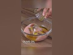 someone is pouring olive oil in a glass bowl on a wooden table with other ingredients