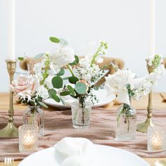 the table is set with white flowers in mason jars, candles and napkins on it