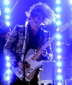 a man with long hair playing an electric guitar in front of microphones and lights