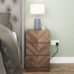 a night stand with a lamp on top of it next to a bed in a bedroom