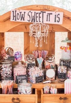 a wooden table topped with lots of candies and candy bar items next to a sign that says how sweet it is