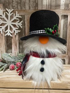 a snowman wearing a top hat and scarf on a wooden table next to a christmas ornament