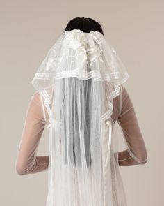 the back of a woman wearing a veil with white flowers on it's head