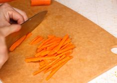 a person cutting up carrots on top of a wooden cutting board with a knife