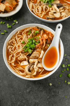 two white bowls filled with noodles and vegetables next to chopsticks on a table